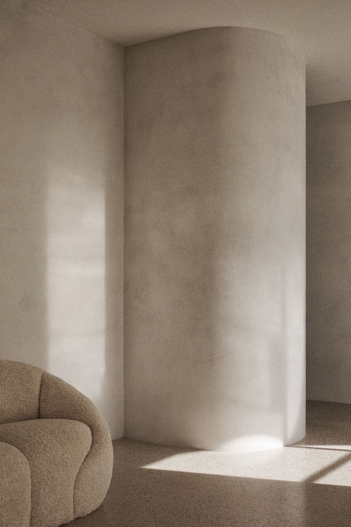 Curved plaster wall meeting warm light over a soft bouclé chair